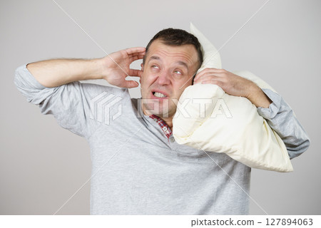 Sleepy man with pillow closing his ear Sleepy man with pillow closing his ear 127894063