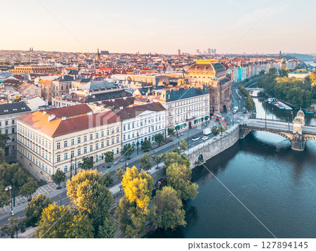 Smetana's Embankment along the Vltava River showcases stunning architecture and vibrant city life in Prague during a beautiful sunset. The scenic river reflects the surrounding historic buildings. 127894145