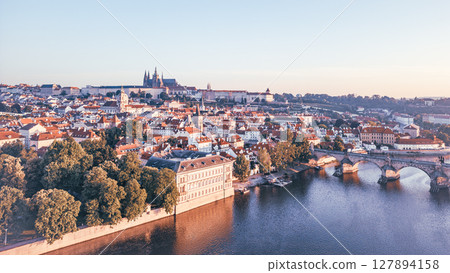 Morning light casts a warm glow on Prague's medieval cityscape, revealing the iconic Charles Bridge and Hradcany Castle along the Vltava River. A breathtaking aerial view captivates. Morning light casts a warm glow on Prague's medieval cityscape, revealing the iconic Charles Bridge and Hradcany Castle along the Vltava River. A breathtaking aerial view captivates. 127894158