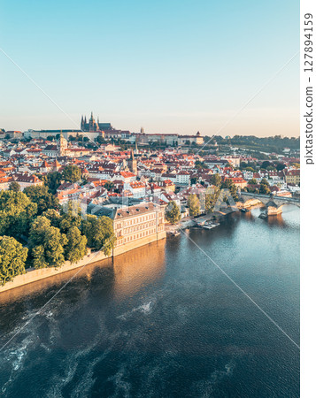Experience the breathtaking sunrise illuminating Prague, as golden light casts over the Vltava River and highlights the iconic Charles Bridge and Hradcany Castle. 127894159