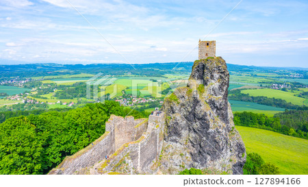 Nestled in the scenic Bohemian Paradise, Trosky Castle Ruins stand atop a rocky outcrop, offering stunning views of the lush green landscape and distant villages under a clear sky. 127894166