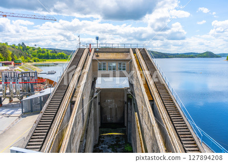 View of the impressive boat lift at Orlik Dam, which efficiently elevates vessels between different water levels. The location features serene water and lush greenery under a partly cloudy sky. View of the impressive boat lift at Orlik Dam, which efficiently elevates vessels between different water levels. The location features serene water and lush greenery under a partly cloudy sky. 127894208