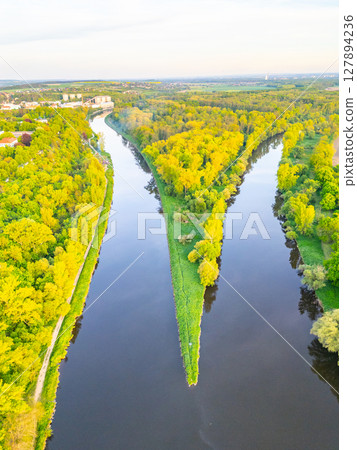 Aerial view showcases the meeting point of Vltava and Labe rivers, surrounded by lush greenery near Melnik. The natural landscape highlights the river bends and vibrant foliage. 127894236