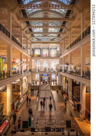 Crowds of people wander through the spacious halls of the Science Museum in London. Bright lights and exhibits capture the interest of visitors throughout the day. 127894252