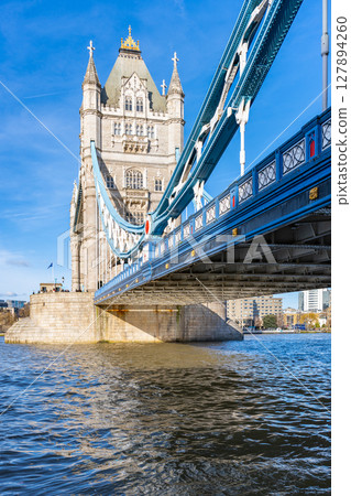 The iconic Tower Bridge in London showcases its architectural beauty under a clear blue sky. The bridge spans the River Thames, reflecting its historic significance and stunning design. 127894260