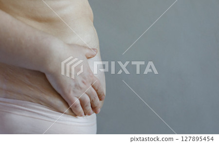 Woman. Belly close up on gray background with copy space. Diet, weight loss, overweight Woman. Belly close up on gray background with copy space. Diet, weight loss, overweight 127895454