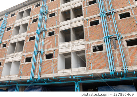 Unfinished building under construction with exposed red brick walls and visible blue PVC plumbing pipes 127895469