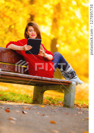 Woman in autumn park using tablet computer reading. 127895738
