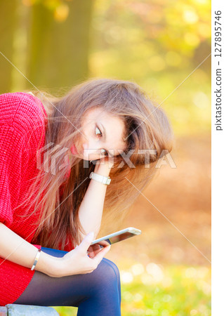Sad girl in park with mobile phone 127895746