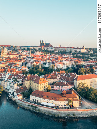 A stunning aerial view of Prague Castle towering above the picturesque Lesser Town, with the Vltava River gracefully flowing through the vibrant cityscape during golden hour. A stunning aerial view of Prague Castle towering above the picturesque Lesser Town, with the Vltava River gracefully flowing through the vibrant cityscape during golden hour. 127895957