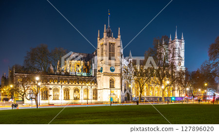Illuminated Westminster Abbey stands tall against the night sky in London. Surrounding trees and lamp posts frame the majestic structure, showcasing its architectural beauty. Illuminated Westminster Abbey stands tall against the night sky in London. Surrounding trees and lamp posts frame the majestic structure, showcasing its architectural beauty. 127896020