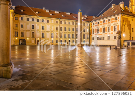 The Mrakotin Monolith stands tall in the courtyard of Prague Castle, surrounded by historic buildings. Soft lamp light reflects off the wet cobblestones, creating a serene nighttime atmosphere. 127896021