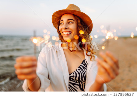The sparklers in hands of young woman on the beach. Woman enjoying party on beach with sparklers. The sparklers in hands of young woman on the beach. Woman enjoying party on beach with sparklers. 127896627