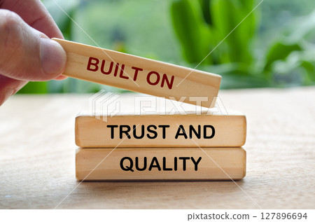 Hand placing wooden block that says Built On Trust And Quality text on Quality Hand placing wooden block that says Built On Trust And Quality text on Quality 127896694