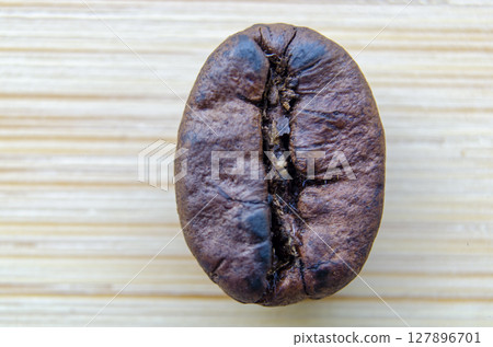 Singular coffee bean with a distinct purple tint and subtle glossiness captured in extreme detail on a light wooden background Singular coffee bean with a distinct purple tint and subtle glossiness captured in extreme detail on a light wooden background 127896701