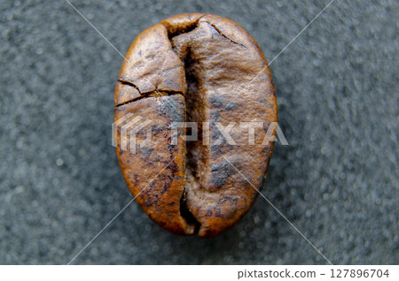 A crisp and detailed closeup shot of a roasted coffee bean displaying its natural texture and deep brown color on a dark gray surface 127896704