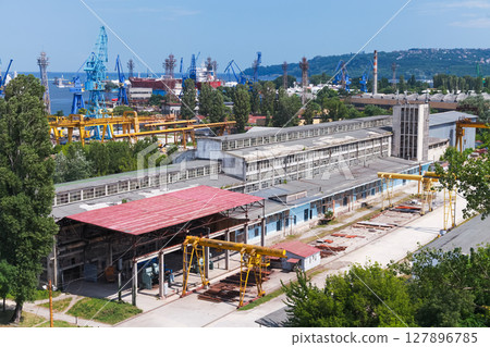View of a large industrial area featuring a factory building, cranes, and a shipyard 127896785