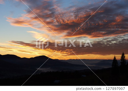 Breathtaking sunset paints sky with vibrant hues of pink, orange, purple, blending into blue morning sky. Silhouetted mountains, pine trees create serene backdrop. Tranquil and picturesque landscape. Breathtaking sunset paints sky with vibrant hues of pink, orange, purple, blending into blue morning sky. Silhouetted mountains, pine trees create serene backdrop. Tranquil and picturesque landscape. 127897007