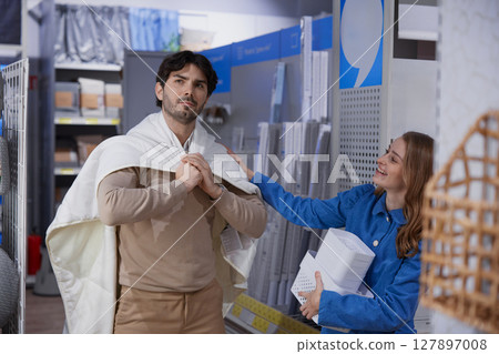 Lovely couple enjoying a fun and playful shopping interaction while choosing a blanket Lovely couple enjoying a fun and playful shopping interaction while choosing a blanket 127897008