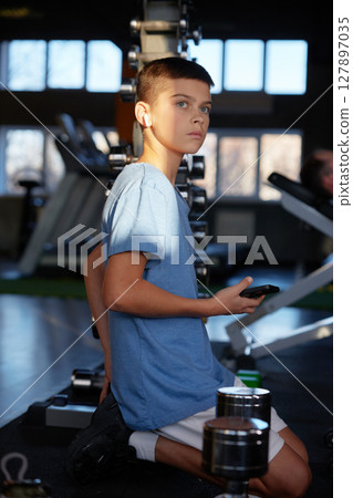 Teen boy with phone searching training video tutorial for sport activity at gym 127897035