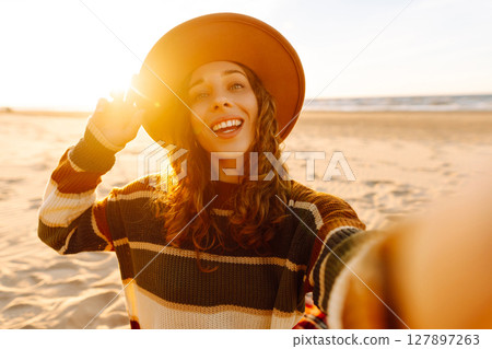 Young woman taking a cheerful selfie on a sandy beach during sunset. Lifestyle, travel, active life 127897263