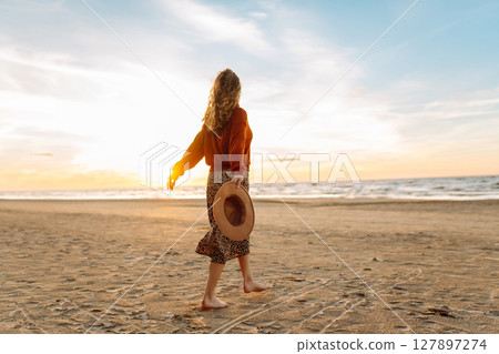 Stylish woman walks at sunset along beach of sea on at sunset. Travel, relax and lifestyle concept. 127897274