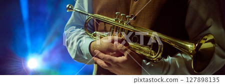 Musician holding trumpet with vibrant stage lights in background Musician holding trumpet with vibrant stage lights in background 127898135