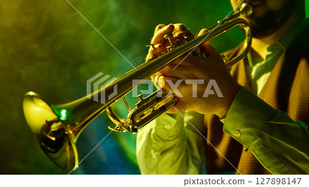 Musician playing trumpet in vibrant green and yellow atmospheric stage lighting 127898147