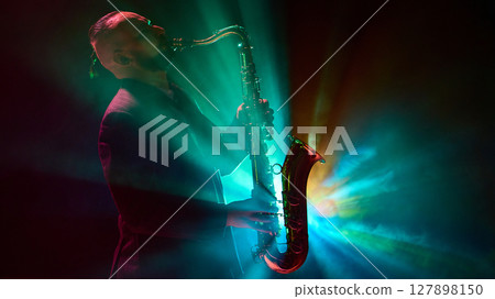 Musician silhouetted playing saxophone with colorful stage lights in dramatic concert setting 127898150