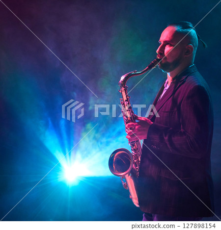 Saxophonist performing on stage with colorful lights and smoke in background 127898154