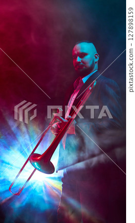 Musician illuminated by colorful stage lights while playing trombone in smoky atmosphere 127898159