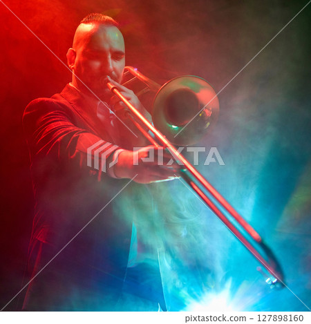 Jazz musician playing trombone under colorful stage lighting and fog effects 127898160