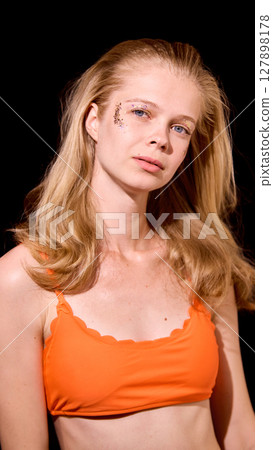 Bold Y2K. Blonde woman with temporary butterfly tattoo wearing orange tank top against black background Bold Y2K. Blonde woman with temporary butterfly tattoo wearing orange tank top against black background 127898178