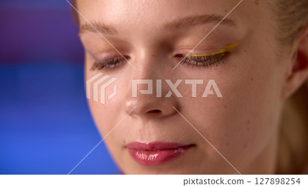 Dopamine makeup. Woman with artistic yellow eyeliner against soft blue background 127898254