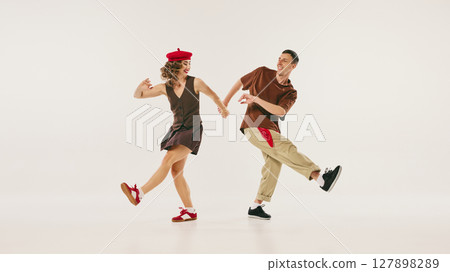 Retro duo performing energetic lindy hop dance move in vintage-inspired outfits on white background 127898289