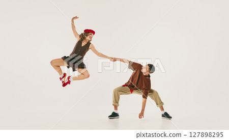 Energetic lindy hop dancers performing high jump in vintage-inspired attire against neutral backdrop Energetic lindy hop dancers performing high jump in vintage-inspired attire against neutral backdrop 127898295