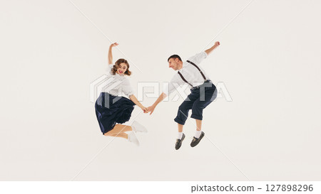 Young couple joyfully performs retro lindy hop dance jump against plain white background Young couple joyfully performs retro lindy hop dance jump against plain white background 127898296