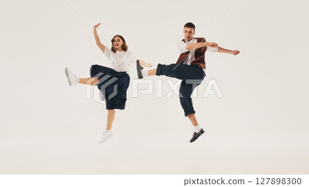 Couple joyfully performing mid-air lindy hop dance move against neutral background 127898300