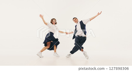 Two people joyfully performing lindy hop dance in retro-inspired outfits against neutral background Two people joyfully performing lindy hop dance in retro-inspired outfits against neutral background 127898306