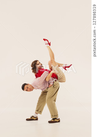 Dancers performing energetic lindy hop maneuver in retro attire on plain background 127898319