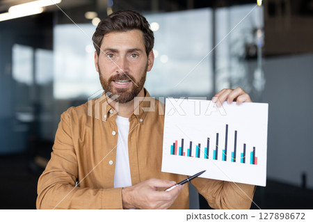 A businessman in a video call presents a chart, highlighting business growth with a pen, suitable for online presentations A businessman in a video call presents a chart, highlighting business growth with a pen, suitable for online presentations 127898672