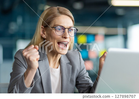 Businesswoman expressing excitement and success at work. Joyful reaction captured in modern office setting with professional attire. Concept of achievement and positive business outcome. Businesswoman expressing excitement and success at work. Joyful reaction captured in modern office setting with professional attire. Concept of achievement and positive business outcome. 127898707