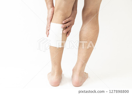 一名男子的腿上有敷料,白色背景 一名男子的腿上有敷料,白色背景 127898800