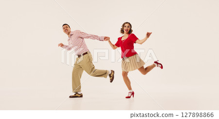 Couple joyfully performing retro lindy hop dance on plain background in vintage attire Couple joyfully performing retro lindy hop dance on plain background in vintage attire 127898866