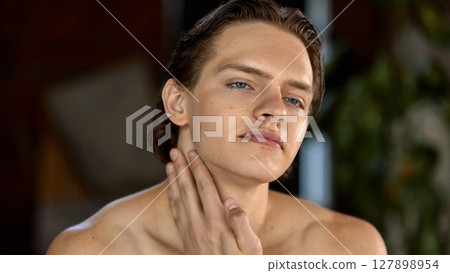 Young man gently applying skincare cream on neck in bright natural setting Young man gently applying skincare cream on neck in bright natural setting 127898954