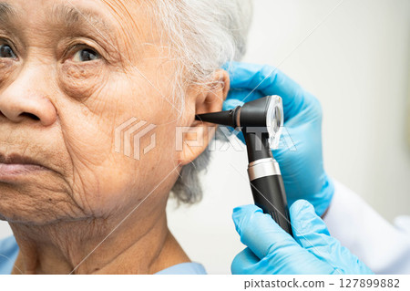 Otolaryngologist or ENT physician doctor examining senior patient ear with otoscope, hearing loss problem. 127899882