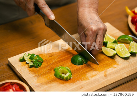 Close-up of man's hand cutting lemon on wooden cutting board in kitchen, preparing for cooking. 127900199