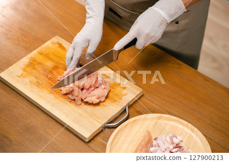 Close-up of Asian man's hands cutting chicken on a wooden cutting board in the kitchen, preparing for cooking. Close-up of Asian man's hands cutting chicken on a wooden cutting board in the kitchen, preparing for cooking. 127900213