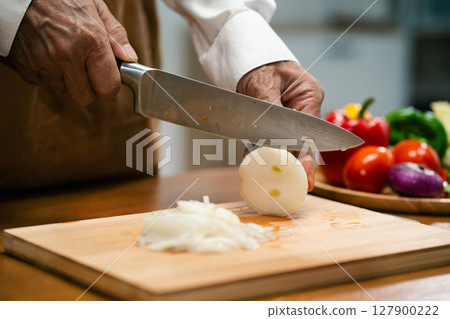 Close up of Asian man's hands cutting onions on a wooden cutting board in a kitchen, preparation for cooking. 127900222