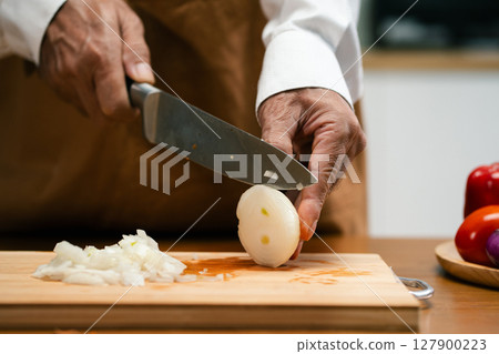 Close up of Asian man's hands cutting onions on a wooden cutting board in a kitchen, preparation for cooking. Close up of Asian man's hands cutting onions on a wooden cutting board in a kitchen, preparation for cooking. 127900223